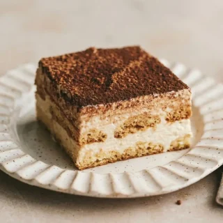 Keto tiramisu layered with coffee-soaked ladyfingers, velvety mascarpone cream, and dark cocoa powder dusting.